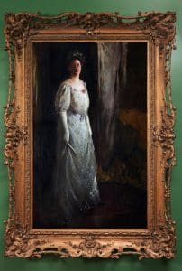 Portrait of a woman in a Victorian style, white gown in an elaborately carved frame.